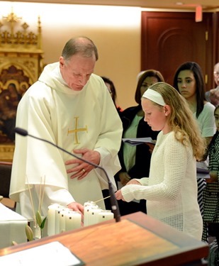 Deacon Geoffrey Higgins assists Katherine Larsen to light a candle for Maureen Mannion